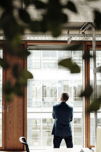 Male business professional looking through window in office