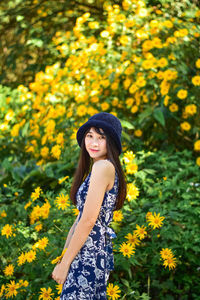 Beautiful young woman standing by yellow flowering plants