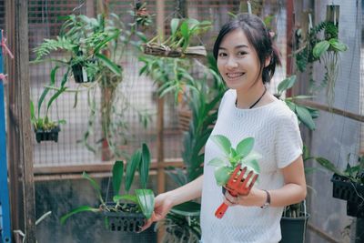 Portrait of young woman examining plants in greenhouse