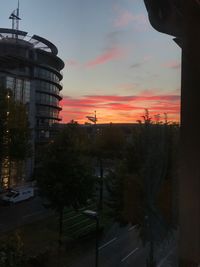 Silhouette buildings by road against sky during sunset