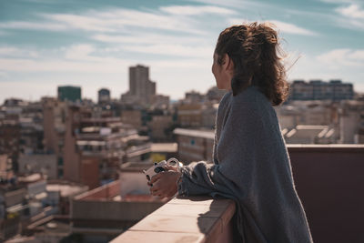 Side view of woman looking at cityscape while standing on terrace