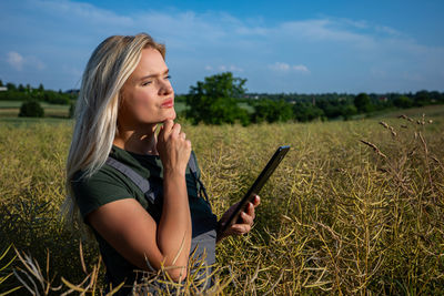 Young woman using mobile phone on field against sky