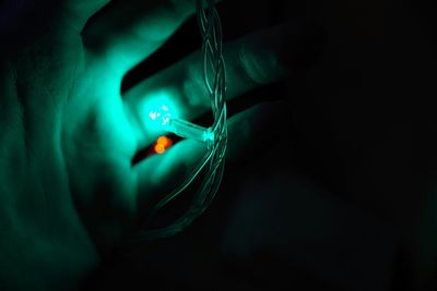 Close-up of hand on illuminated string light in darkroom