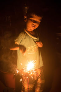 Little boy holding lit sparkler at night