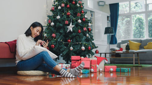 Young woman sitting by christmas tree on floor at home
