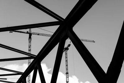 Low angle view of cranes seen through metallic structure against sky
