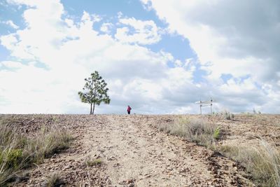 Distant view of man standing on field against cloudy sky