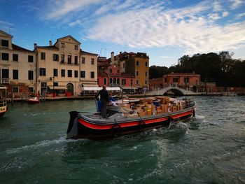 Boat in canal by buildings against sky