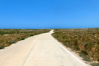 Road amidst field against clear blue sky