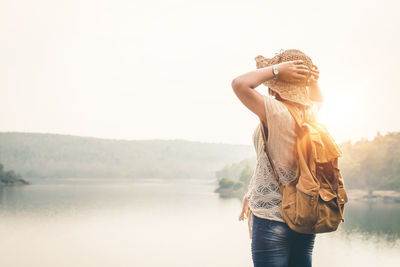 Midsection of woman standing by lake against sky