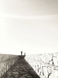 People walking on footpath against clear sky