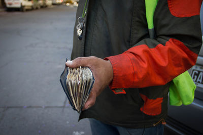 Midsection of man holding paper currencies on road