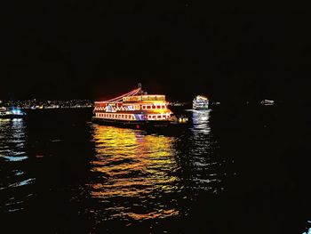 Illuminated city by sea against sky at night