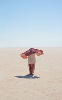 Rear view of woman standing at desert against clear sky