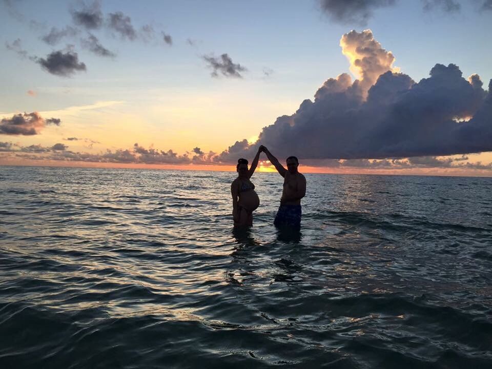 SILHOUETTE PEOPLE IN CALM SEA AGAINST SKY DURING SUNSET