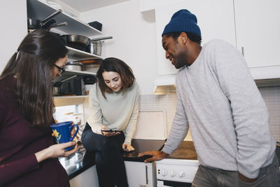 Young woman showing mobile phone to roommates in kitchen