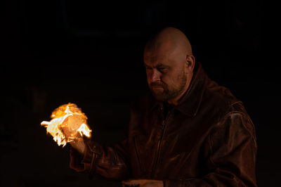 Man holding burning candle against black background