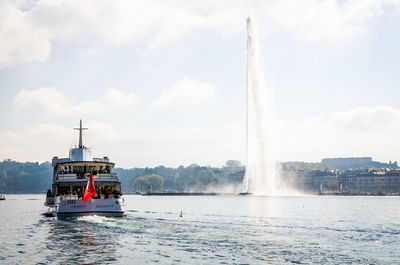 People sailing in boat by fountain in lake against sky