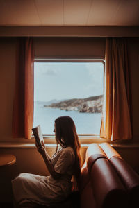 Rear view of woman sitting at window