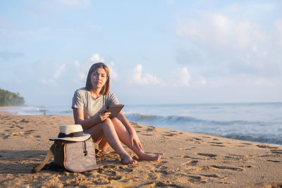 Young woman sitting on shore at beach against sky