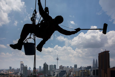 Low angle view of silhouette window washer working against sky