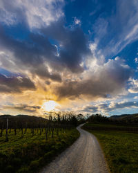 Road amidst field against sky during sunset