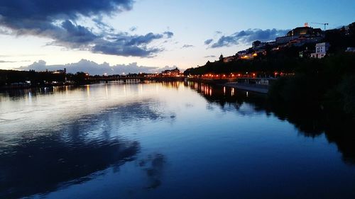 River by illuminated city against sky at dusk