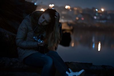 Woman sitting at illuminated park against sky at night