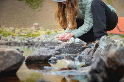 Young girl fills the palms of her hands with water from a stream of a cold mountain lake