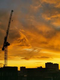 Silhouette crane by building against orange sky