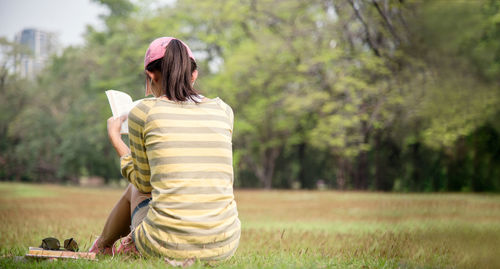 Rear view of woman reading book while sitting on field