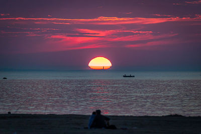 The golden sun rising above lighthouse and fisherman in the ocean.