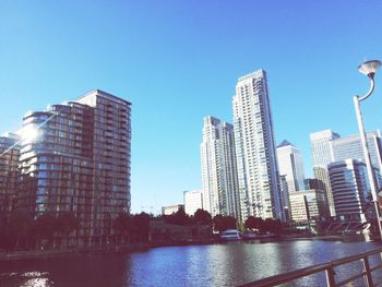 Skyscrapers by river against clear blue sky