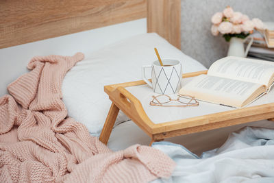 Cup of coffee, book and glasses on bed with soft blanket indoors