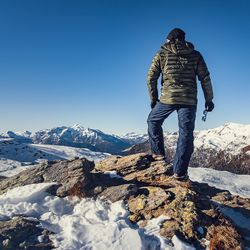 Rear view of mid adult man standing on snowcapped mountain against clear blue sky