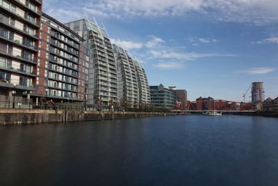 Buildings by river against sky in city