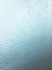 Close-up of water drops on glass against sky