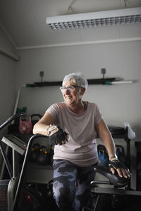 Happy senior woman leaning on exercise bike at health club