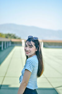 Portrait of smiling young woman standing at building terrace against sky