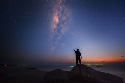 Silhouette of man standing and pointing towards sky at night