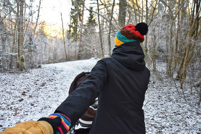 Rear view of woman wearing knit hat walking in snow covered forest