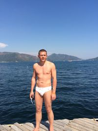 Portrait of shirtless young man standing on pier over sea against clear sky