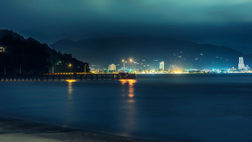 Illuminated buildings by sea against sky at night