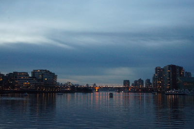 Illuminated city by sea against sky at night