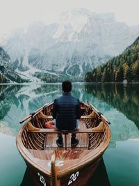 Rear view of young man sitting on boat in lake against mountains