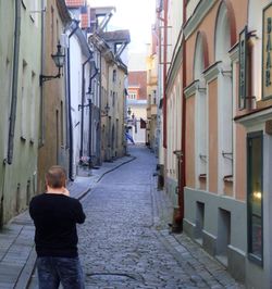 Rear view of man standing on footpath amidst buildings