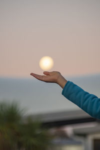 Person holding moon over  cloud against sky during sunset 