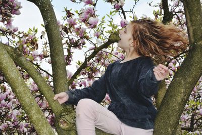 Side view of woman sitting by flower tree