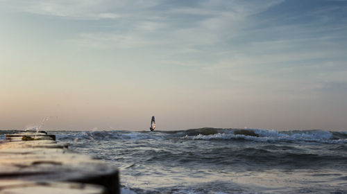 Man standing in sea against sky during sunset