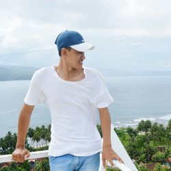 Young man wearing cap while standing against sea